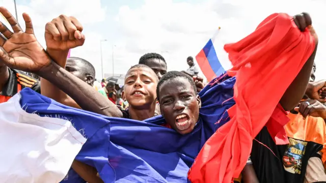 A man wrapped in a Russian flag waves his arms and shouts as supporters of Niger's military leaders gather to protest outside Nigerien and French air bases in Niamey on August 27, 2023.