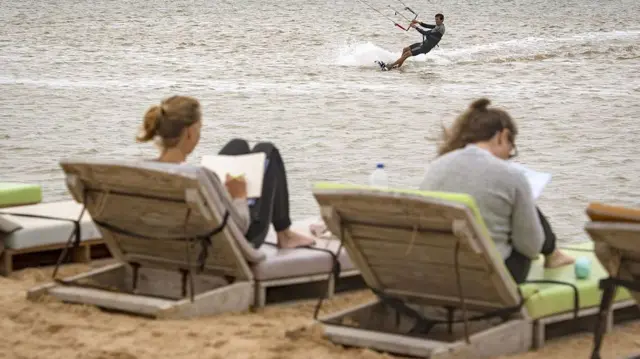 European tourists relaxing on sun loungers in Western Sahara while another engages in kitesurfing in the sea